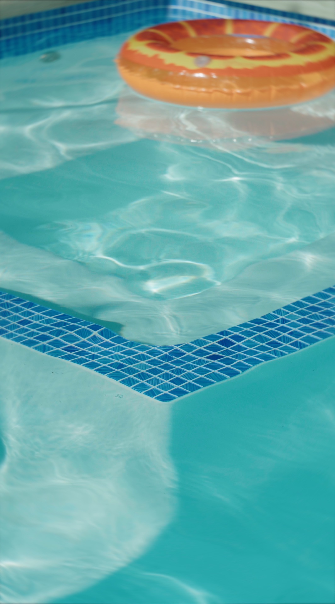 Detalhe da borda pastilhada da piscina sob a água, com uma boia laranja flutuando