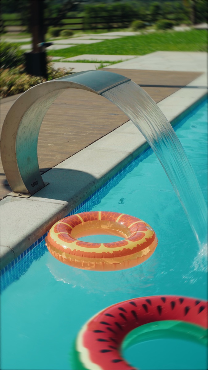 Cascata de inox jorrando na piscina, com boias coloridas na água