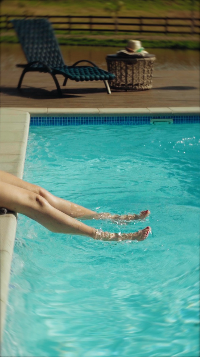 Pessoa sentada na borda da piscina com as pernas na água azul